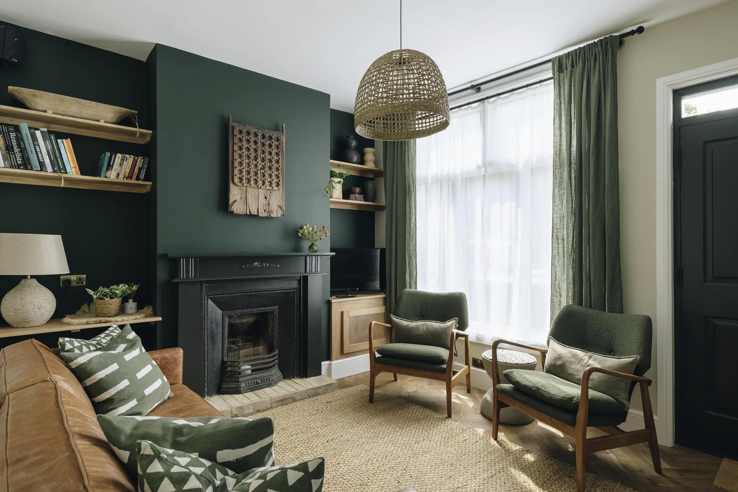 The Plough House living room with a green wall, fireplace and armchairs