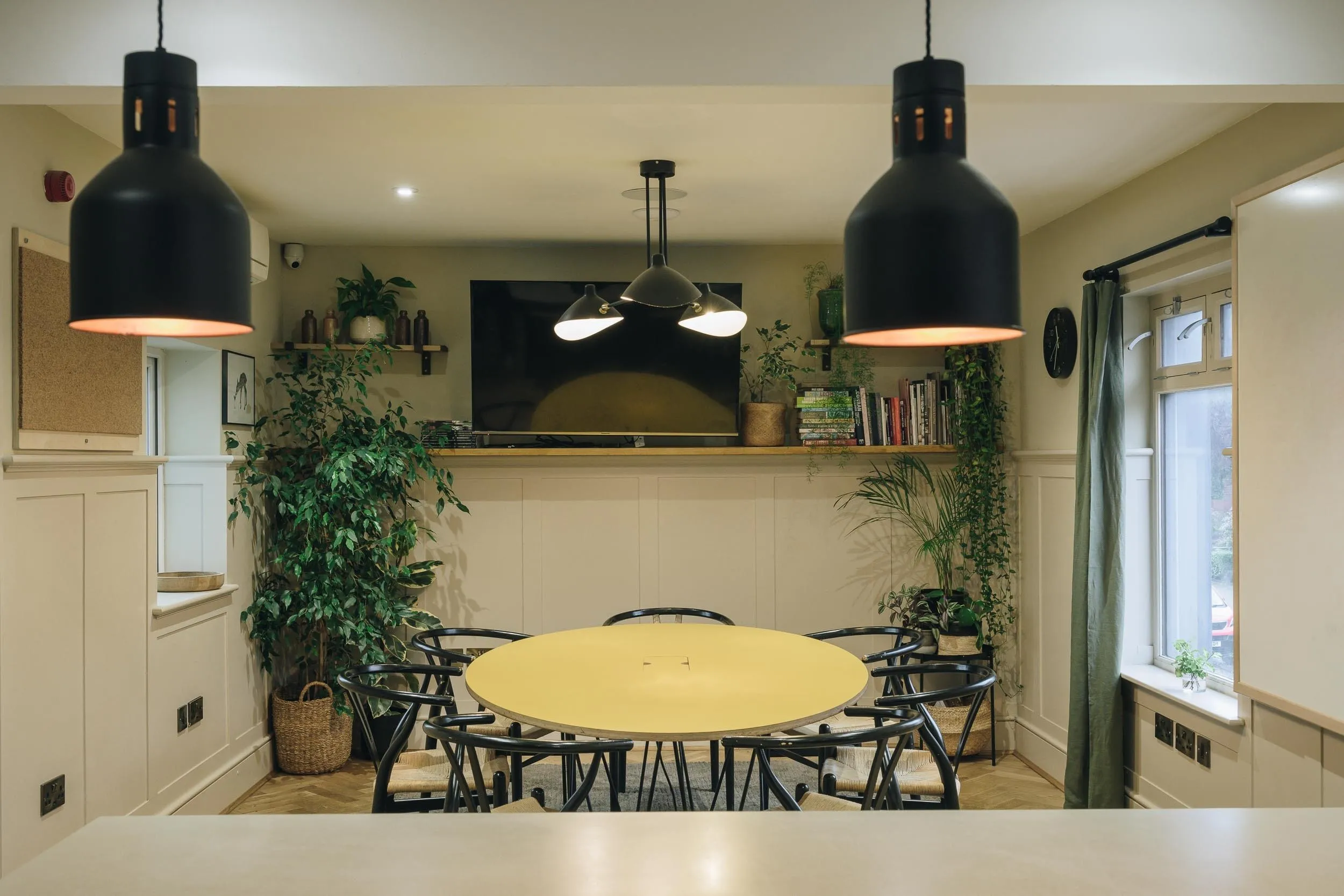 The Studio round table with eight chairs below a wall-mounted TV