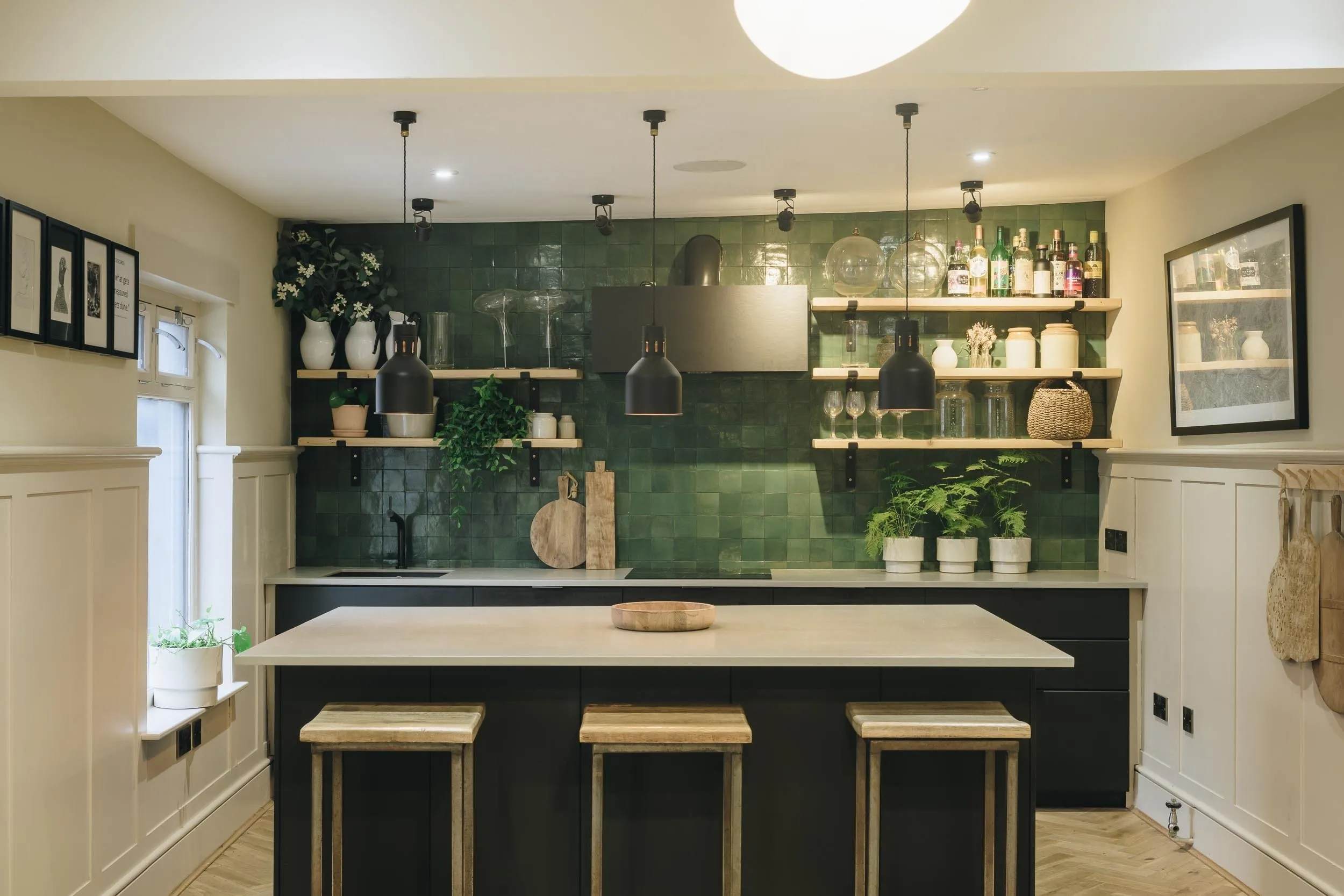 The Studio kitchen with green tiled wall, open shelves and bar stools at the island